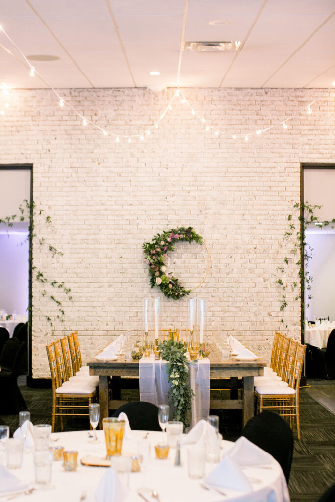 Decorated wooden table and chairs in front of a white brick wall at a wedding reception.