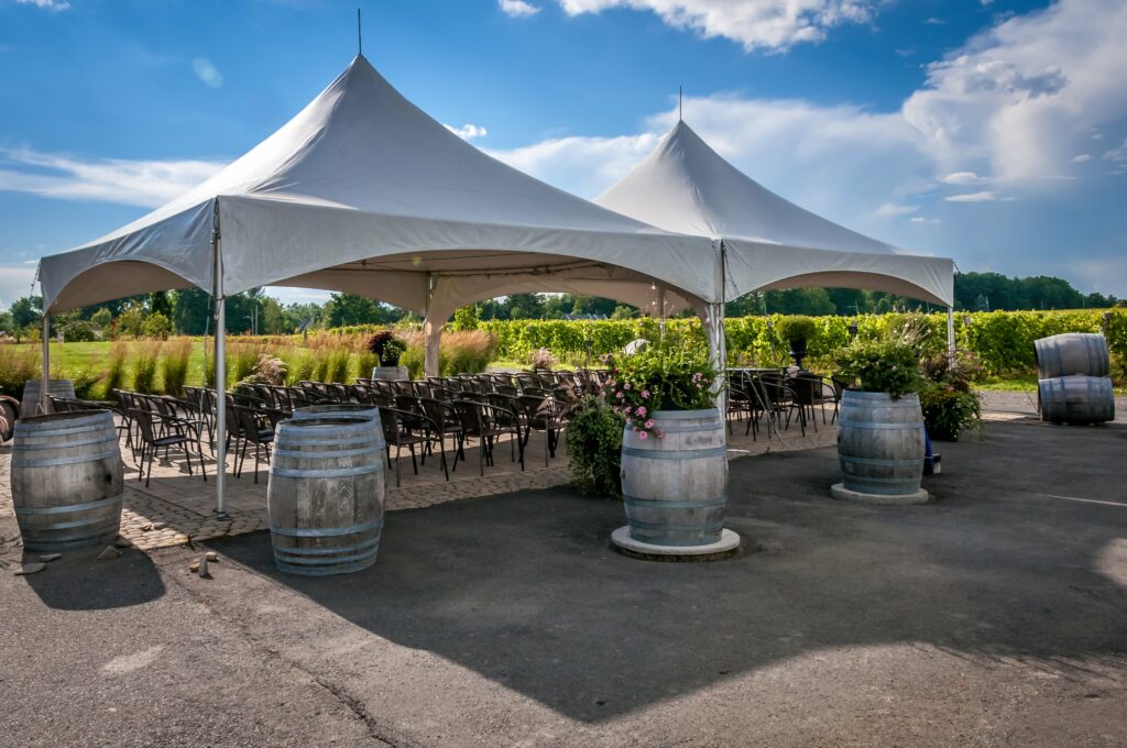 Outdoor wedding ceremony set up under canopy tents with wine barrels placed around the tents.