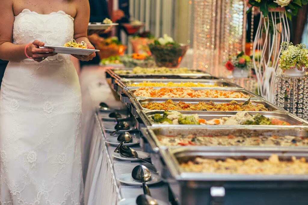 Bride walking down buffet line while holding a plate.