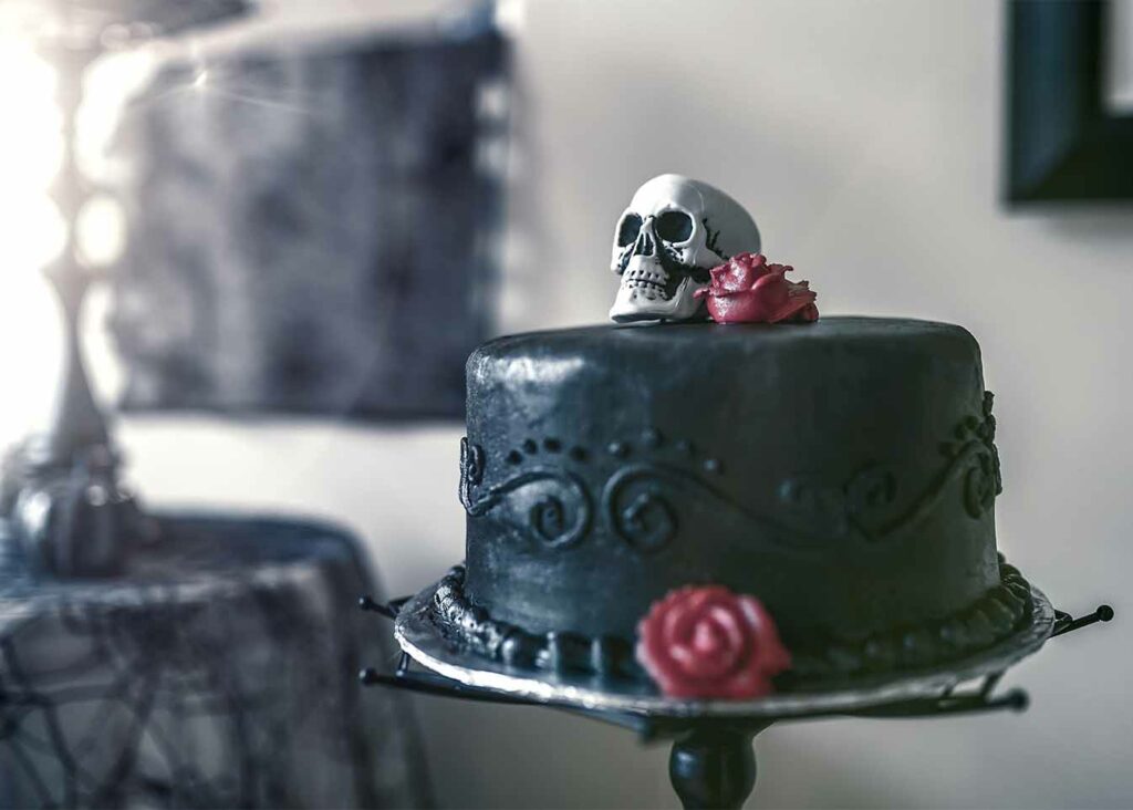 Black wedding cake with a skull and red rose on top displayed on a spider web cake stand.