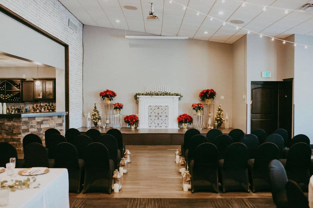 Indoor wedding ceremony setting with red roses and black chair covers.